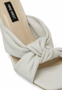 White leather high-heeled sandal featuring a knotted design at the front, open toe, and smooth texture. Logo label visible inside.