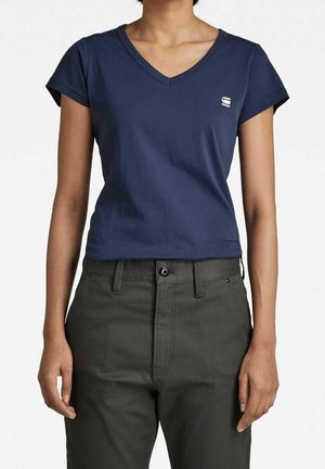 Camiseta de manga corta con cuello en V de color azul marino, hecha de algodón, con un pequeño logo blanco en el pecho, combinada con pantalones de tiro alto grises.