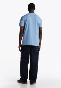 T-shirt azzurro chiaro a maniche corte con taglio dritto e una trama sottile, abbinato a pantaloni cargo blu navy scuri con tasche laterali.