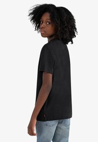 Svart bomull t-skjorte med korte ermer, rund hals og rett kant. Merkbar rød etikett detalj på venstre side. Brukes sammen med lyseblå jeans.