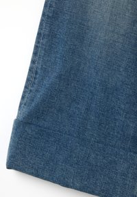 Puño de tela de mezclilla de un par de jeans, en un tono azul medio, con una superficie texturizada y corte recto en el dobladillo.