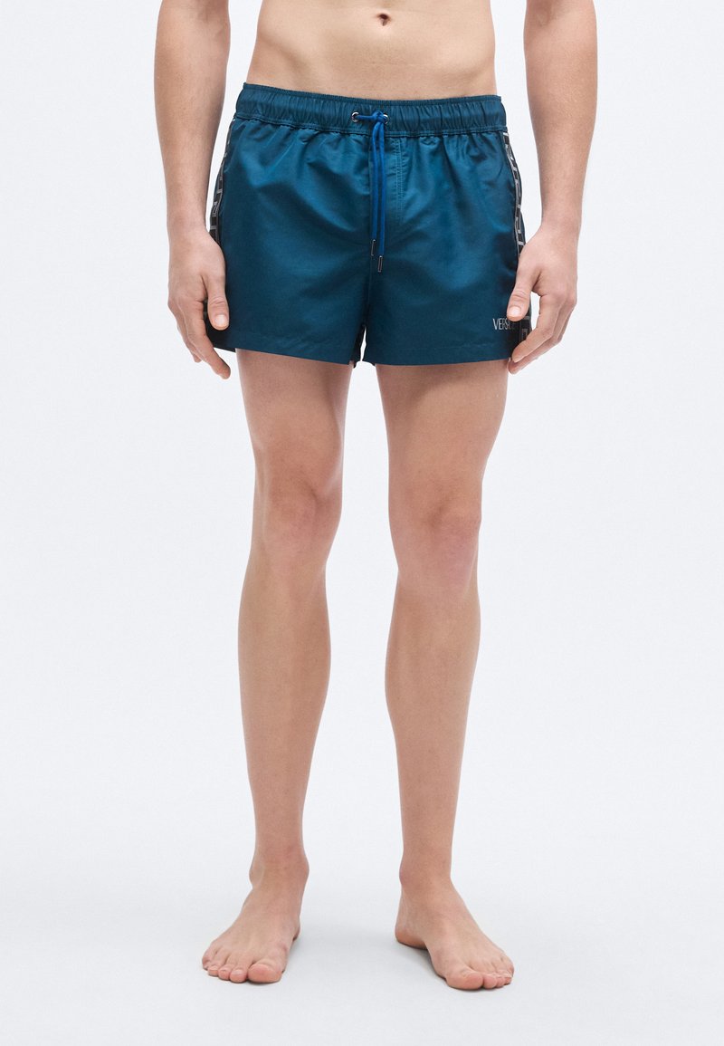 Τιρκουάζ μαγιό βερμούδα με κορδόνι στη μέση και ρίγες στα πλάγια. Κατασκευασμένο από ελαφρύ ύφασμα, με μικρό λογότυπο μπροστά.