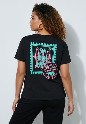 Frau mit lockigem Haar trägt ein schwarzes T-Shirt mit türkis-pinkem Sardinen-Druck und portugiesischem Poststempel auf dem Rücken.
