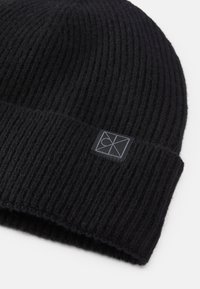 Gorro de malha preto feito de lã texturada, apresentando uma dobra na parte inferior e um pequeno logo preto cosido na frente.