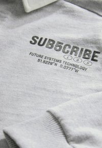 Grijze katoenen sweatshirt met een witte kraag en zwarte opdruk: "SUB5CRIBE LDN FUTURE SYSTEMS TECHNOLOGY 51.5228°N 0.0777°W."