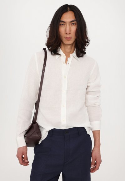 Fehér vászon ing hosszú ujjakkal, gombos előlappal és gallérral. Sötét tengerészkék nadrággal és egy kis barna bőr keresztpántos táskával viselve.