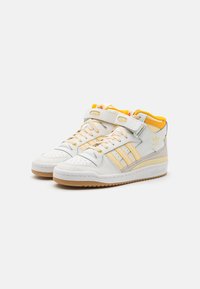 White high-top sneakers crafted from leather, featuring yellow accents, three stripes design, and a Velcro strap. Gum rubber sole.