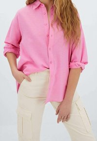 Roze overhemd met knopen, een losse pasvorm en opgerolde mouwen, gecombineerd met crème cargobroek met zijzakken en een gladde textuur.