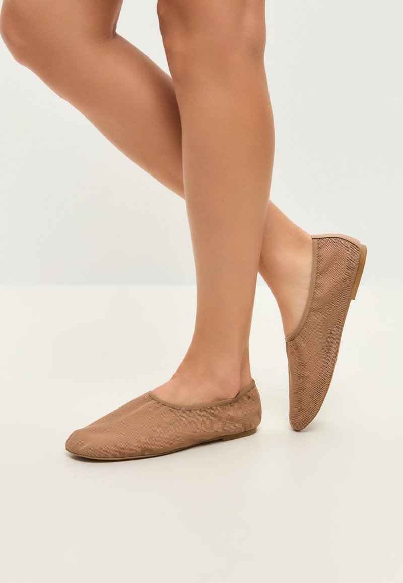 Zapatillas ligeras color beige sin cordones, hechas de un tejido texturizado, con punta redonda y suela plana, que destacan por su diseño minimalista y construcción sin costuras.