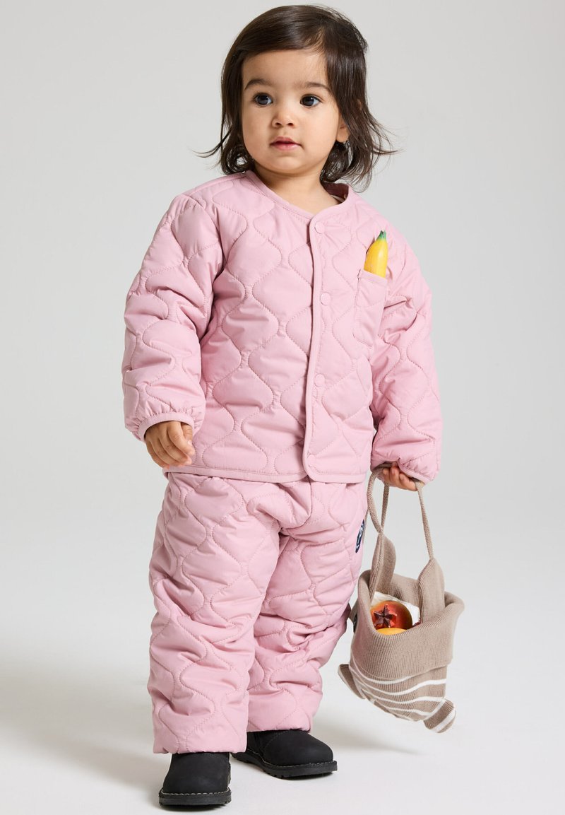 Gestepptes pinkes Kinderoutfit, mit einem gemusterten Textur. Enthält eine Tasche mit einem gelben Gegenstand und einer kleinen beigen Tasche. Schwarze Fußbekleidung.