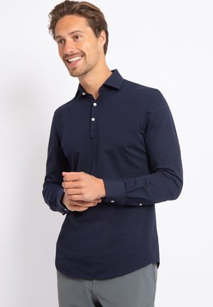 Marineblaue Langarmbluse mit Knopfleiste, weichem Material und abgerundetem Saum. Mit weißen Knöpfen an den Manschetten, taillierte Passform.
