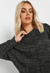 Czarny, teksturowany top o luźnym kroju, z szerokim dekoltem i długimi rękawami. Subtelny wzór dodaje wizualnego zainteresowania.