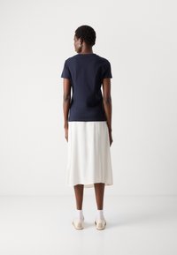 T-shirt azzurro a maniche corte abbinato a una gonna bianca fino al ginocchio. Il modello indossa scarpe chiare e calze bianche, visto da dietro.