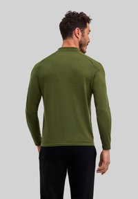 Długa koszula w kolorze oliwkowej zieleni z okrągłym dekoltem, wykonana z gładkiej tkaniny, z płaskimi szwami i luźnym krojem.