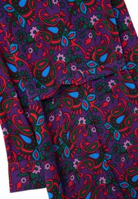 Tissu violet avec un motif floral et des motifs paisley vibrants, comportant des accents rouges, verts, bleus et roses. Boutons visibles sur le vêtement.