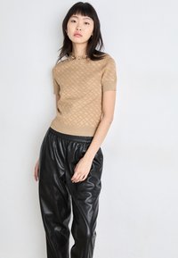Μπεζ κοντομάνικο πλεκτό τοπ με υφασμάτινο σχέδιο, σε συνδυασμό με φαρδιά μαύρα παντελόνια από τεχνητό δέρμα με ελαστική μέση.