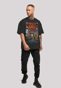 Camiseta negra de gran tamaño con un gráfico colorido de cómic de Batman. El diseño incluye rostros detallados y texto sobre una superficie de tela suave.
