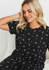 Svarta pyjamasar med ett vitt körsbärsmönster. Mjuk duk med korta ärmar och löst sittande passform. V-ringad design för komfort.