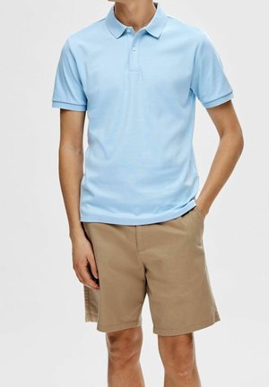 Jasnoniebieska koszulka polo z klasycznym kołnierzykiem i krótkimi rękawami, zestawiona z beżowymi szortami. Tkanina wydaje się gładka i lekka.