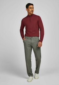 Bordeaux, trui met rits en hoge nek gecombineerd met grijze, gestructureerde broek. Model draagt witte sneakers. Neutrale achtergrond. Focus op de details van de kleding.