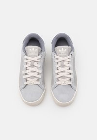 Grå mockaskor med en slät yta, vita snören och en logotyp på tungan. Har en rund tå och en texturerad gummisula.