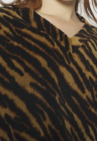 Brązowo-czarny pulower w paski tygrysa z dekoltem w serek, wykonany z miękkiego, teksturowanego materiału o wyraźnym wzorze zwierzęcym.