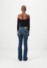 Top negro de manga larga y sin hombros combinado con jeans de denim azul acampanados. Los jeans presentan un parche beige en la parte posterior de la cinturilla y dos bolsillos traseros.