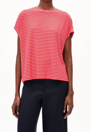 Persoon die een rood-wit gestreept topje met korte mouwen en een zwarte broek draagt, staand met ontspannen armen langs het lichaam.