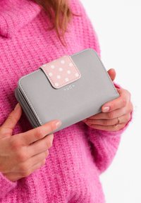 Gray wallet with a pink polka dot clasp, made from textured material, featuring a zip closure. Brand name "VUCH" displayed on the front.