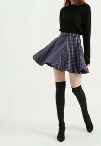 Sukně s vícolorým vzorem houndstooth v modré, růžové a zelené, s rozšířeným střihem, zkombinovaná s černými vysokými botami a černým topem.