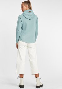 Világoskék kapucnis pulóver pöttyös mintával, off-white színű, bő szárú nadrággal és fekete talpú, fehér bokacsizmával párosítva.