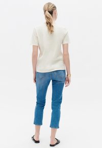 Jasno beżowa, krótko rękawowa koszulka w luźnym kroju, w połączeniu z jasnoniebieskimi, skróconymi dżinsami o lekkim przetarciu oraz czarnymi płaskimi sandałami.