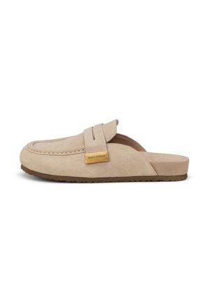 Mocassin beige en daim à enfiler avec semelle en caoutchouc plate et étiquette de marque rectangulaire dorée sur la bride traversant le dessus.