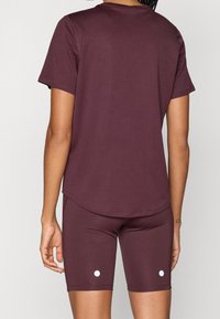 Person klädd i matchande vinröd kortärmad skjorta och cykelbyxor med små vita cirkulära prickar nära fållen, sedd bakifrån.