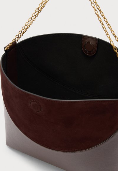 Σκούρο καφέ τσάντα τύπου κουβά με επάνω μέρος από απαλό σουέντ, κάτω μέρος από λείο δέρμα, μαύρη εσωτερική επένδυση, κλείσιμο με μαγνητικό κουμπί και λουριά ώμου αλυσίδα σε χρυσούς τόνους.