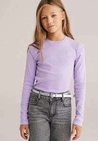 Šviesiai violetinė ilgarankovė marškinėliai su gofruota tekstūra, su mažu siuvinėtu gėlių motyvu. Derinama su aukštakulnėmis pilkomis džinsais ir baltu diržu.