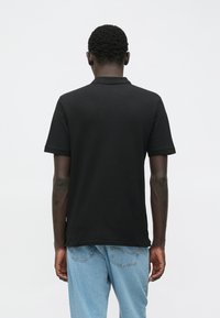 Schwarzes kurzärmliges Poloshirt aus Baumwolle, mit einem klassischen Kragen, geradem Saum und entspannter Passform, kombiniert mit hellblauen Jeans.