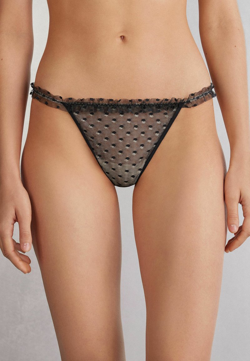 Zwarte mesh string met stippenpatroon, voorzien van een franjerand van kant. Doorzichtige textuur en minimalistisch ontwerp met weinig bedekking.