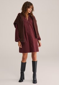 Burgundia nööbiga kleit pikade puhvärvidega ja pruunist koesallist. Mudel kannab kuni põlveni ulatuvaid musti saapaid. Sile kangastekstiur on nähtav.