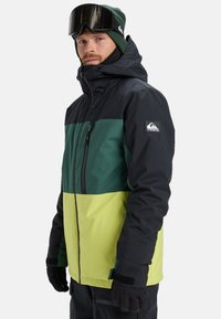 Ski jacket featuring a color-block design with black, green, and bright yellow sections, made from weather-resistant material. Includes zip pockets.