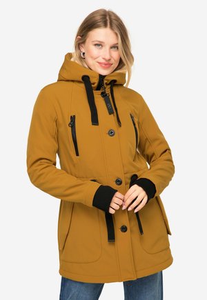 Honigfarbener Softshell-Jacke mit Kapuze, schwarzen Reißverschlusstaschen und verstellbarem Kordelzug in der Taille, mit schwarzen Akzenten und Bündchen.