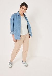 Giubbotto di jeans in blu chiaro, top a righe bianche e pastello, pantaloni cargo beige e sneakers con motivo e accenti grigi e blu.