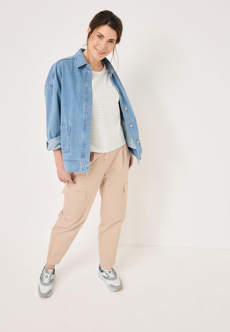 Giubbotto di jeans in blu chiaro, top a righe bianche e pastello, pantaloni cargo beige e sneakers con motivo e accenti grigi e blu.