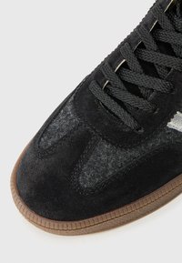 Sneaker in suede nero con accenti in feltro grigio, punta rotonda, lati grigi testurizzati e lacci neri. Suola in gomma con bordi scanalati.