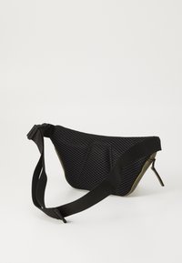 Schwarze Netztasche mit einer geschwungenen Form, die einen glatten olivgrünen Boden, einen verstellbaren Riemen und einen Reißverschlussverschluss aufweist. Sichtbares strukturiertes Oberflächenmuster.