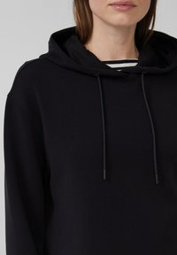 Felpa nera con cappuccio, dal tessuto liscio, dotata di coulisse e con una maglietta a strisce a strati visibile all'apertura del colletto.