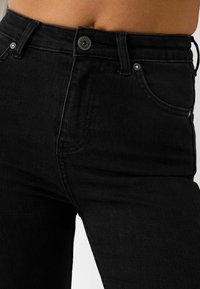 Jeans de mezclilla negros de cintura alta con un diseño clásico de cinco bolsillos, cierre de botón metálico y un sutil desgaste en la textura de la tela.