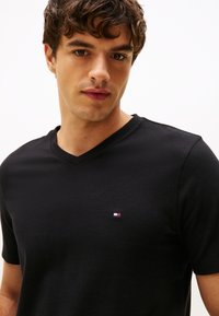 Svart v-ringad t-shirt i bomull, med korta ärmar och en liten broderad logotyp på vänster bröst. Mjuk textur.