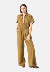 Mono caqui de manga corta, con cremallera frontal, cintura elástica y dos bolsillos en el pecho, combinado con zapatos de estampado animal.