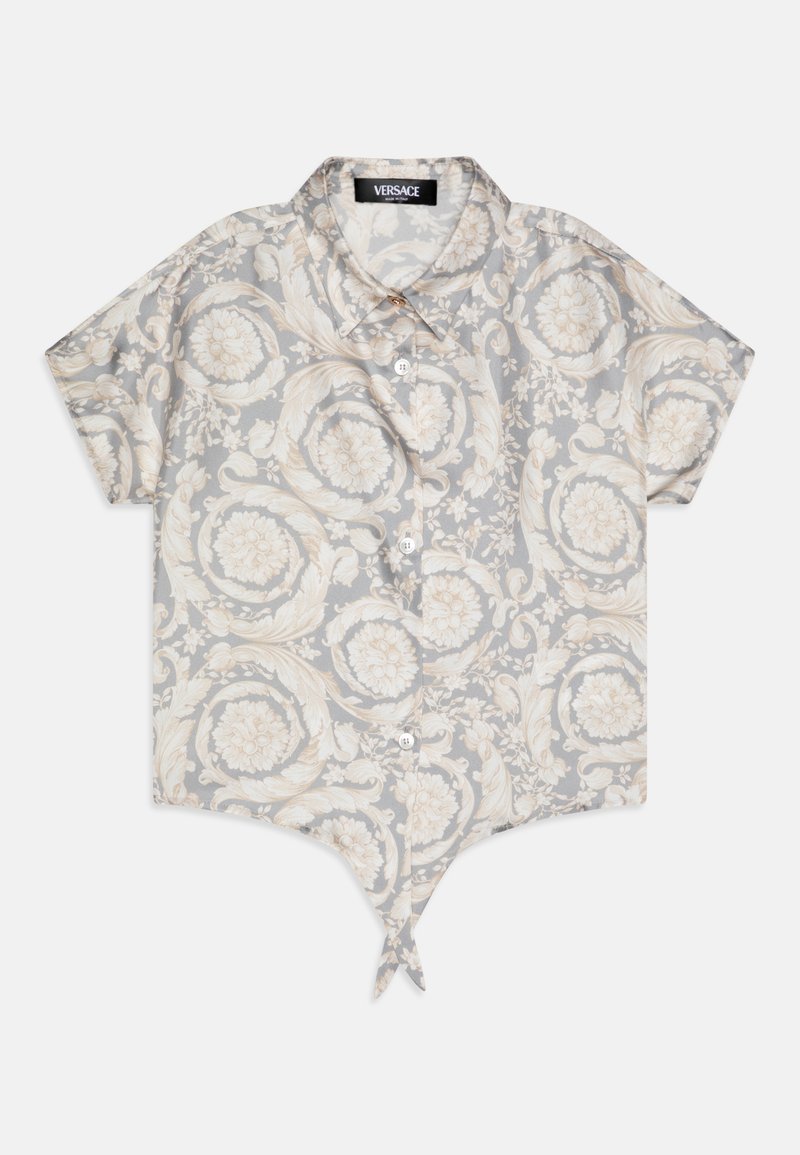 Chemise à manches courtes avec des boutons de couleur gris clair, ornée d'un motif floral en crème. Elle présente un ourlet pointu et un détail de nœud en bas.